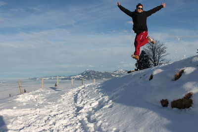 Playful young man jumping on snow covered mountain against sky