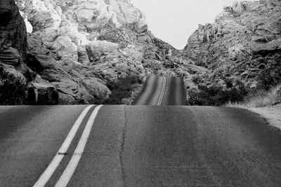 Empty road amidst trees and mountains against sky