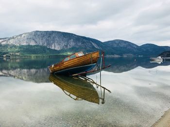 Boat moored on lake by mountains against cloudy sky