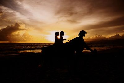 Silhouette people and horse at beach against sky during sunset
