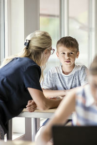 Teacher assisting boy at desk with girl in foreground
