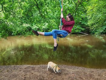 Young woman sitting on rope swing by pond