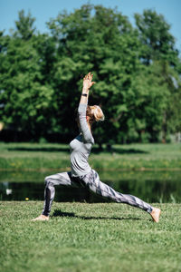 Full length of young woman exercising by pond on field