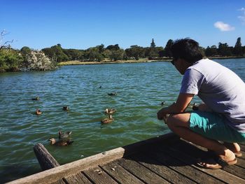 Man sitting on lake against clear sky