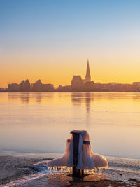 View of bollard by lake against cityscape during sunset