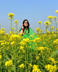 Young woman standing amidst yellow flowering plants on field