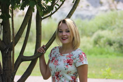 Smiling young woman standing against tree