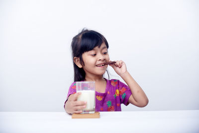 Side view of young woman drinking milk against white background