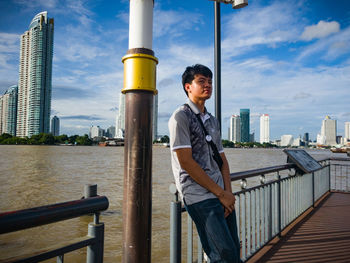 Man looking away while standing by railing against sky