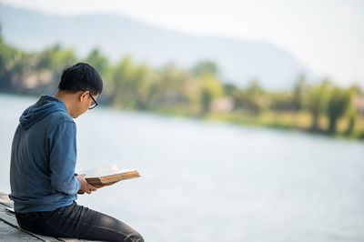 Man reading book while sitting by river