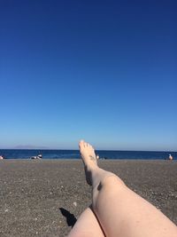 Low section of woman relaxing at beach against clear blue sky