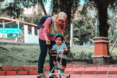 Portrait of smiling woman with daughter on toy scooter playing in park