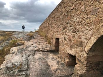 Rear view of man standing on rock against sky