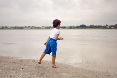 Rear boy child in blue shorts walks by the lake in summer