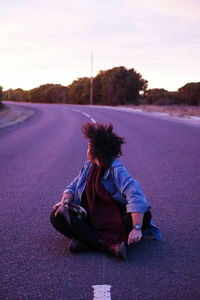 Man sitting on road against sky at sunset