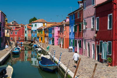 Boats moored in canal amidst buildings against clear sky