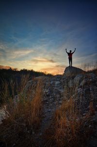 Low angle view of man standing with arms outstretched against sky during sunset