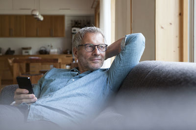 Mature man holding cell phone sitting on couch