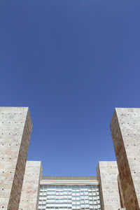 Symmetric architectural structure, with stone texture windows in the center against clear blue sky.