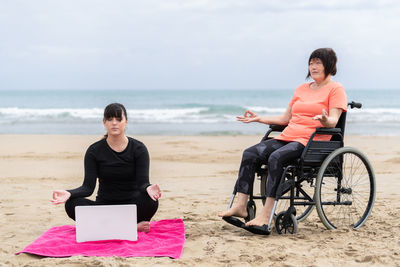 Woman sitting on beach by sea against sky