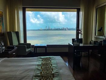 Chairs and table by sea against sky seen through window