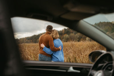 View through car window, man and woman are embracing each other, adult couple enjoying road trip	