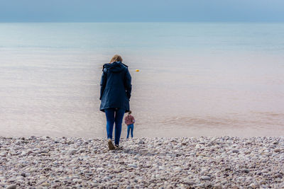 Rear view of woman standing at beach against sky