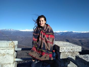 Portrait of smiling woman standing by railing against mountain