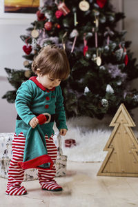 A little 12-month-old christmas elf with a christmas tree and gifts