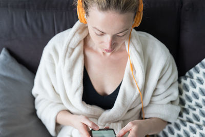 High angle view of woman listening music sitting on sofa at home