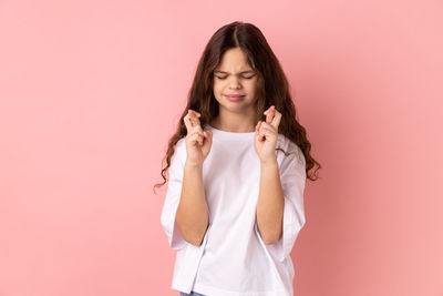 Portrait of young woman standing against pink background