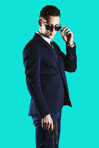 Young man wearing sunglasses standing against blue background