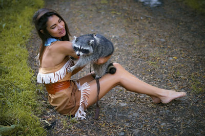 Young woman in traditional clothing playing with raccoon in forest