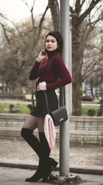 Portrait of young woman standing against pole in city