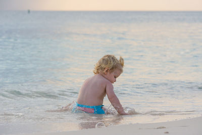 Shirtless boy sitting on shore at beach