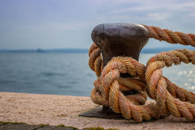 Close-up of rope tied to bollard by sea against sky