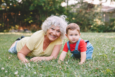 Portrait of smiling grandmother with grandson on grassy land in park