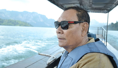 Man wearing sunglasses sitting in boat on lake against sky