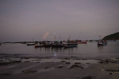 Sailboats moored on sea against sky at dusk