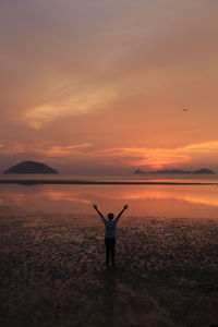 Rear view of man standing on shore against sky during sunset