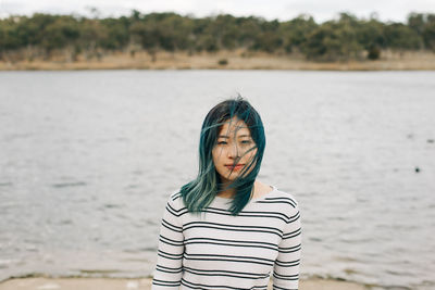 Portrait of young woman standing by lake