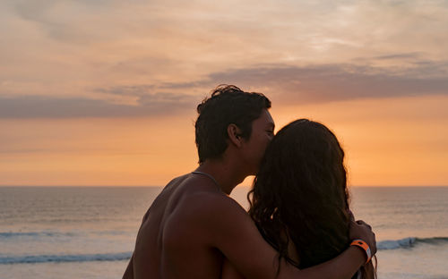 Couple kissing against sea during sunset