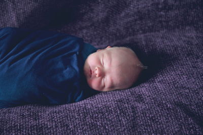 High angle view of newborn sleeping on purple fabric