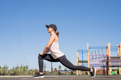 Happy woman in sportclothes working out on the sports ground in sunny summer day, warming up