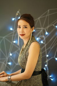 Portrait of beautiful woman sitting against illuminated lights 