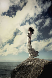 Low angle view of woman standing on rock against sky