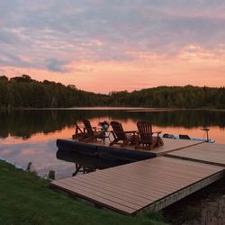 Adirondack chairs on pier over lake during sunset