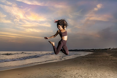 Young woman jumping at sunset on the beach expressing her joy of living. late summer atmosphere.