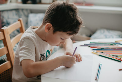 The boy draws with pencils at the kitchen, closeup. high quality photo