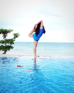 Rear view of woman stretching at beach against sky